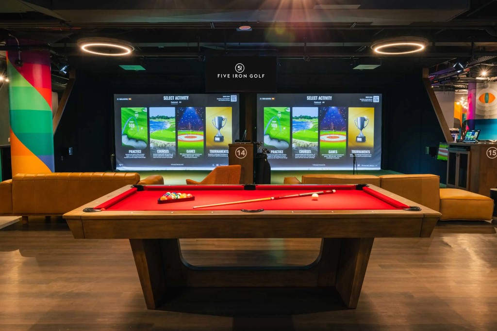Leather lounge seating and a pool table in front of two Trackman simulator bays.